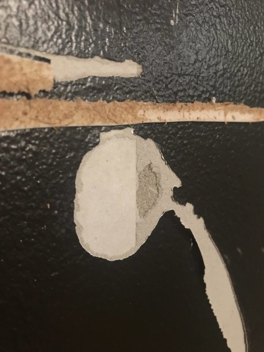 Gipsvägg med skadat område där limrester och bortdragen kartong syns efter borttagen panel.