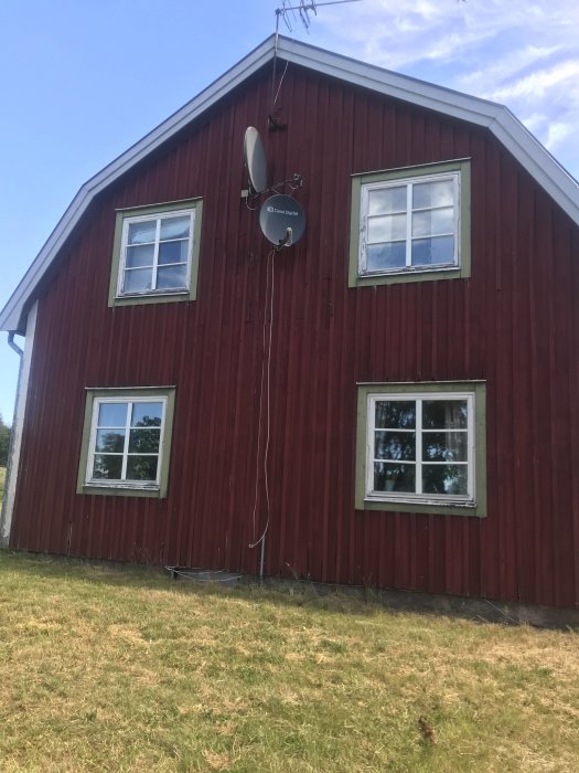 Röd träfasad på ett hus med vita fönsterramar och en satellitdisk, fråga om att måla om från falurött.