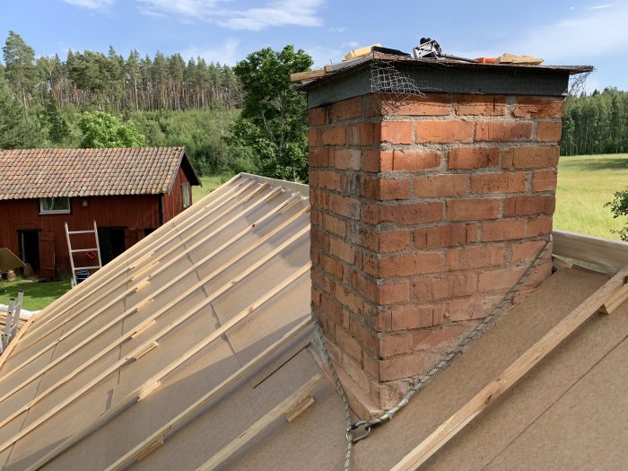 Nyinstallerade taksparrar med ströläkt och trekantslister nära en skorsten på ett hus under renovering.