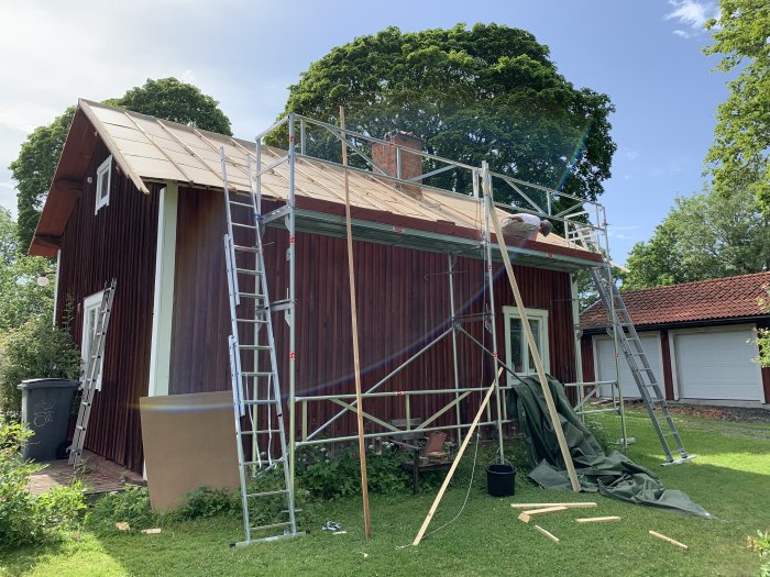 Renovering av ett rödfärgat hus med pågående arbete på taket med ställningar och byggmaterial synligt.