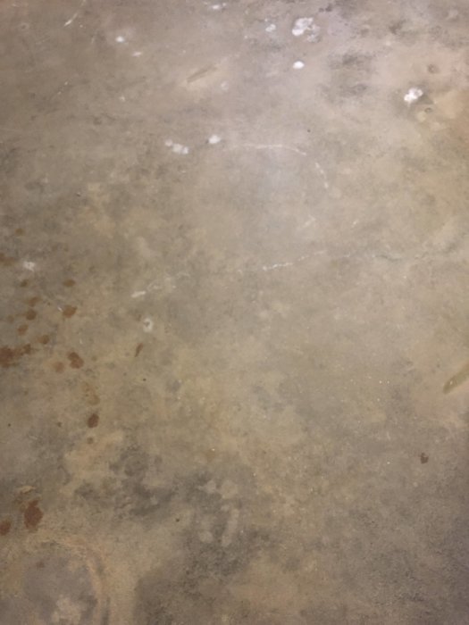 Orenat betonggolv i källare med fläckar och vita avlagringar.