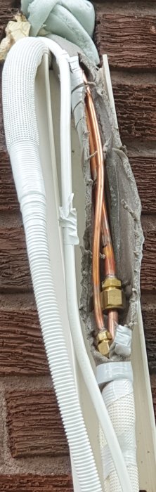 Anslutning på värmepumps utsida med kopparledningar, isolering och kablar.