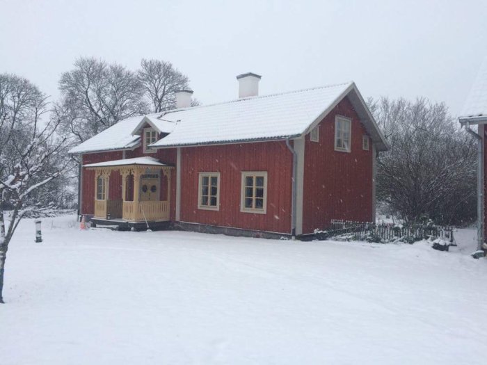 Rött trähus med snickarglädje och enkelglasfönster täckt av snö, som exemplifierar traditionellt varsamt renoverat arv.