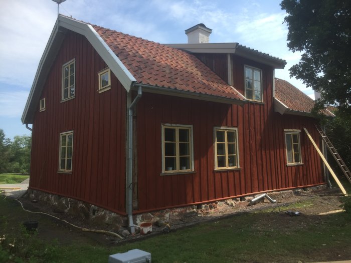 Rödfärgat gammalt hus under varsam renovering med traditionella fönster och en stege mot fasaden.