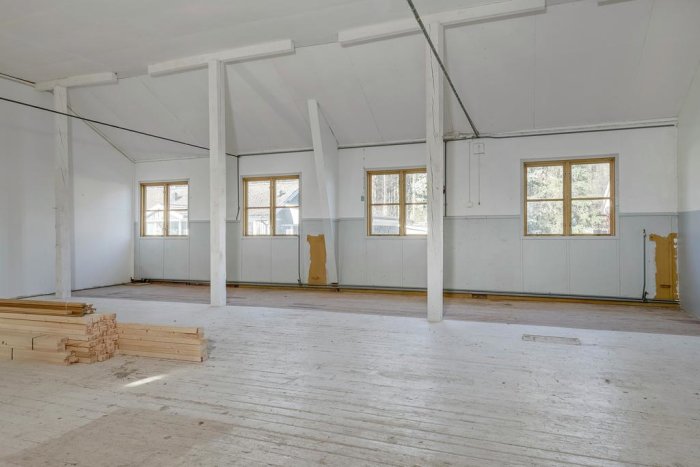 Interiör av en tom byggnad med vita väggar, sliten trägolv och synliga vajrar över taket.