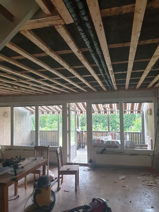 Renoveringsarbete i progress med synliga takreglar, nedrivet tak, och byggverktyg i ett tomt rum.