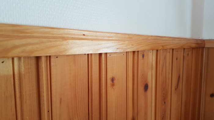 Träpanel och list vid ett väggmöte, halvblank finish, skillnad i lyster syns.