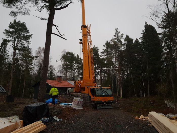 Mobilkran vid byggarbetsplats för tillbyggnad med material och arbetare i bakgrunden.