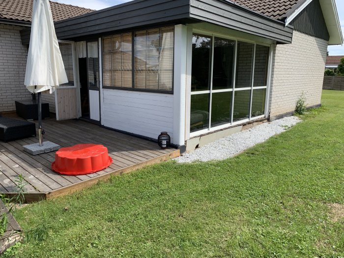 Trätrall med möbler framför hus med skjutdörrar, lekande gräsmatta till höger.