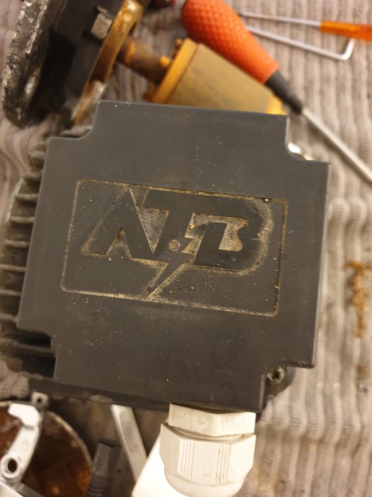 Närbild av en motor med ett dammigt svart ellock märkt med "ATB", omgiven av verktyg och delar av en Pahlen pump.