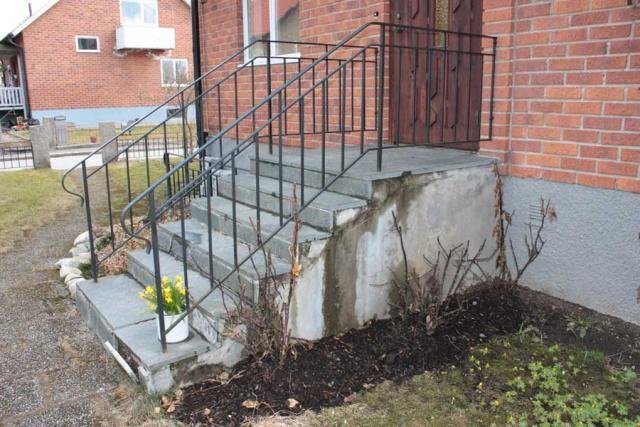 Kiviset portaat, joissa on metallikaide, graniittilevyjä ja kulunut betonipinta. Pieni kukkaryhmä portaiden sivulla.