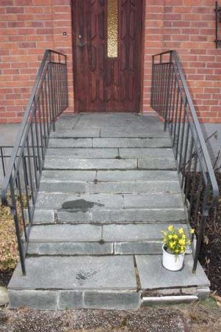 Graniittiportaat, joissa metalli kaiteet, rapautunut betonialusta ja keltainen kukka ämpärissä etureunassa.