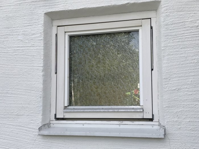 Fönster med texturerat glas i en vitmålad vägg, omgiven av en vit karm.