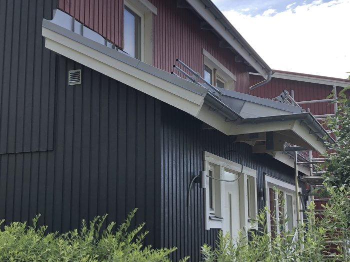 Vindskivor och kantplåtar installerade på ett hus med röd vindskiva och svart fasad.