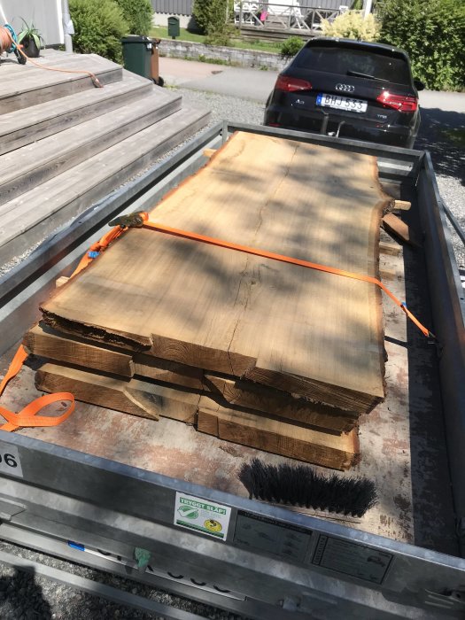 Tjocka plankor av trä säkrade med orange spännband på släpvagn.