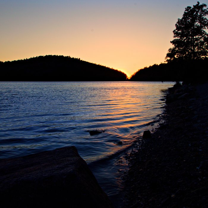 Solnedgång vid en klippig strand på västkusten med lugnt vatten.