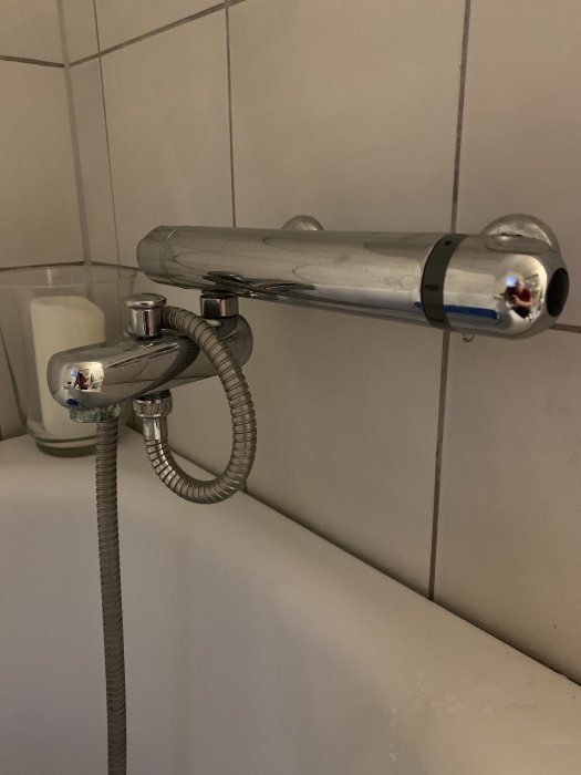 Kromad duschblandare med temperaturkontroll som läcker, monterad på kakelvägg ovanför en badkarskant.