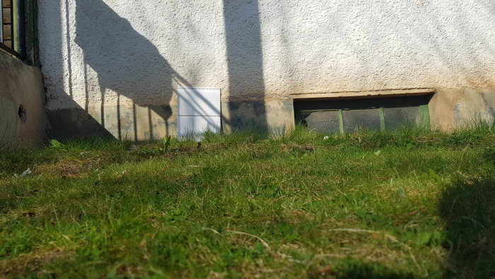 Exempel på liggande panel på husvägg, sedd nära marknivå i solljus med gräs i förgrunden.