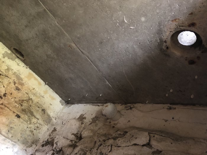 Jordkällare under renovering med synliga ventilationsrör i taket och äldre murverk.