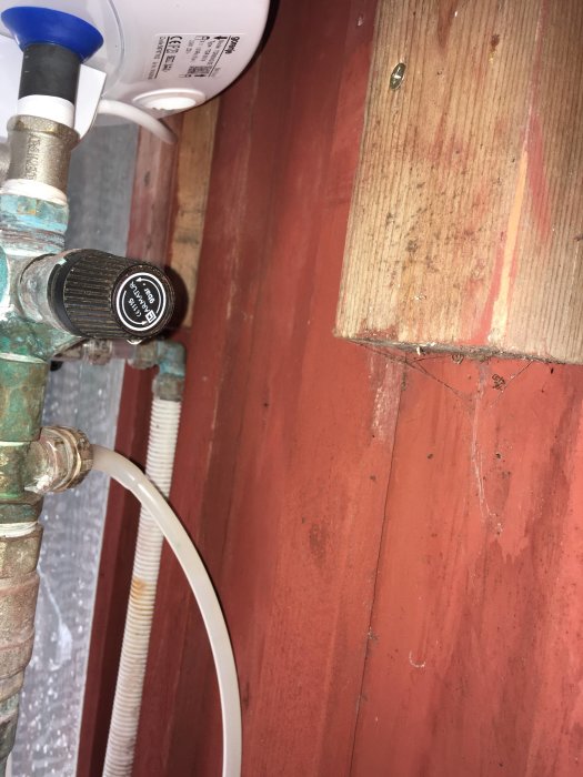 Vit tryckpump kopplad till kopparrör med kran märkt "CE1115 Lk Armatur 9bar" vid röd vägg.