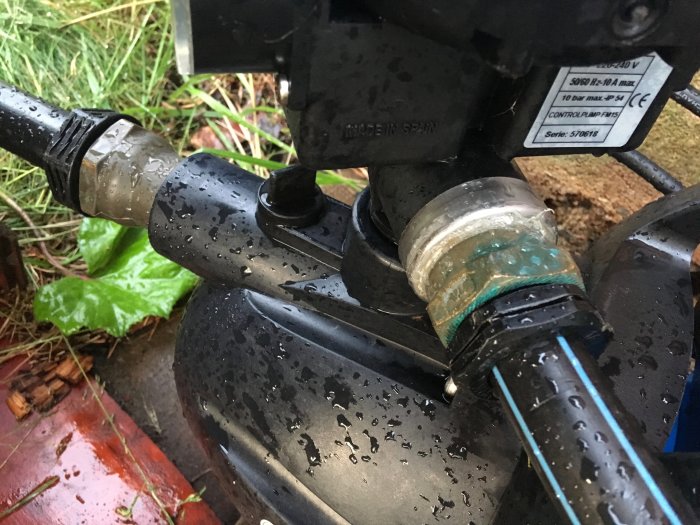 Närbild av mässingskoppling monterad på rör med vattendroppar, del av pumpsystem.