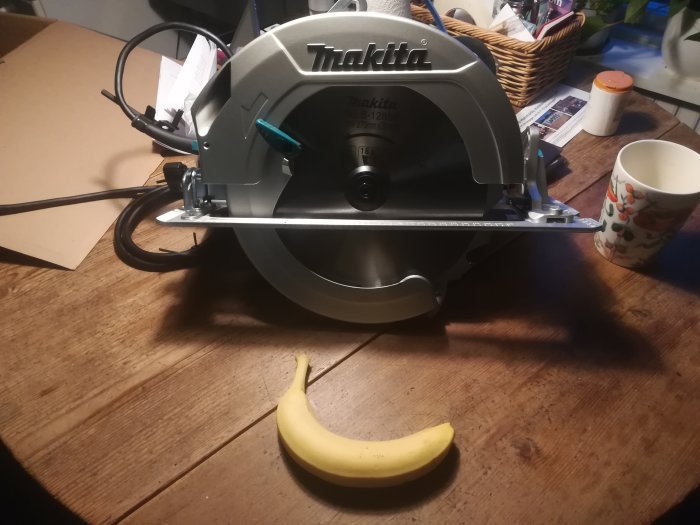 En ny Makita cirkelsåg på ett träbord med en banan och kopp till höger.