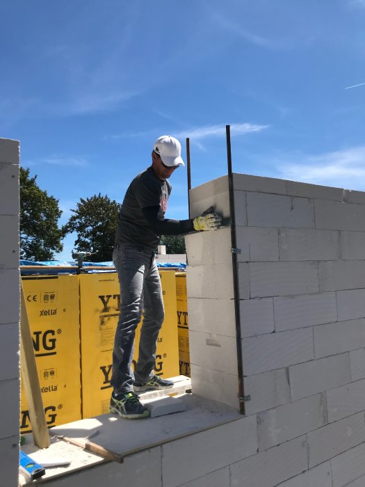 Person bygger en vägg med Ytong lättbetongblock vid huskonstruktion under klarblå himmel.