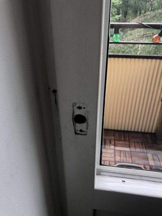 En balkongdörr med ett demonterat lås och synliga skruvhål mot en bakgrund med utsikt över en balkong.