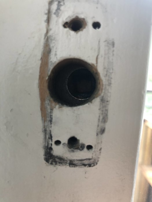 Slitet låshus med en rund, urborrad cylinder och skruvhål i en dörr.