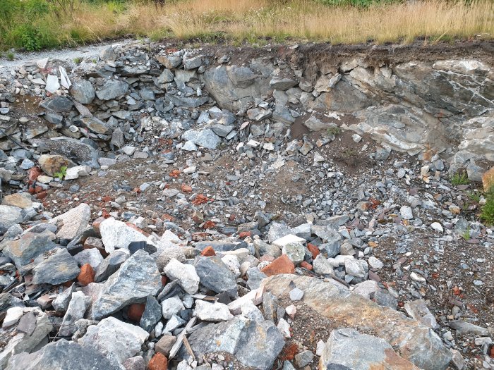 Stenig och ojämn grop i marken med blandade stenstorlekar och synlig berggrund.