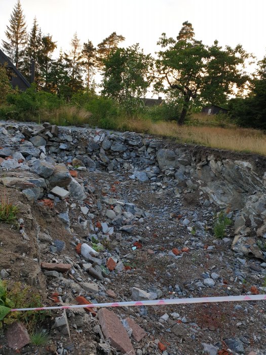 En grop på 10 x 2 meter med klippor och bråte omgiven av grönska och träd.