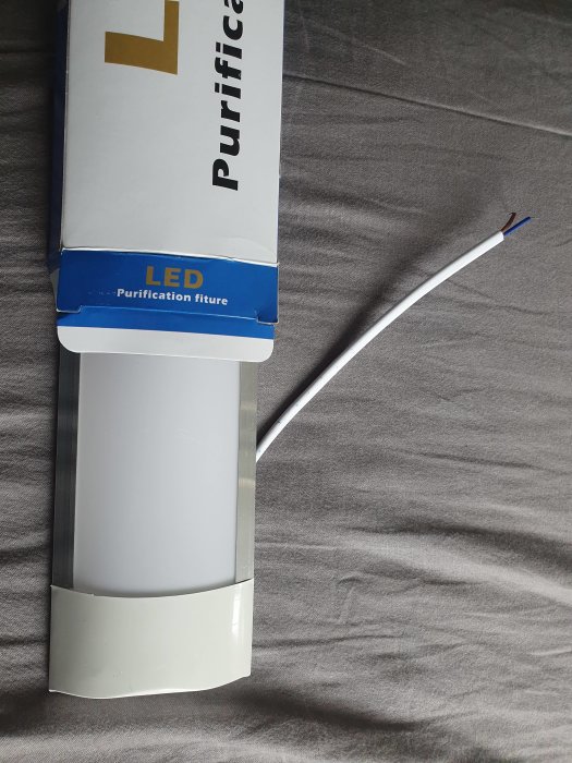 LED-armatur med tunn anslutningskabel uttagen ur förpackning på tygunderlag.