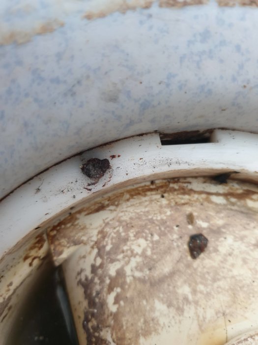 Närbild av en rostig och smutsig golvbrunn ring med en avbruten skruv, tecken på långvarig försummelse.