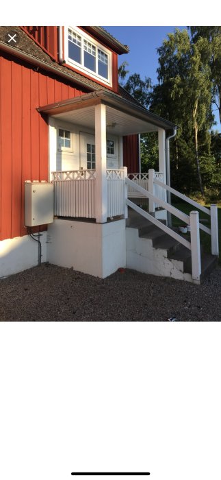 Bild på rödmålat hus med vit veranda och en vit trappa som visar tecken på slitage och sprickbildning.