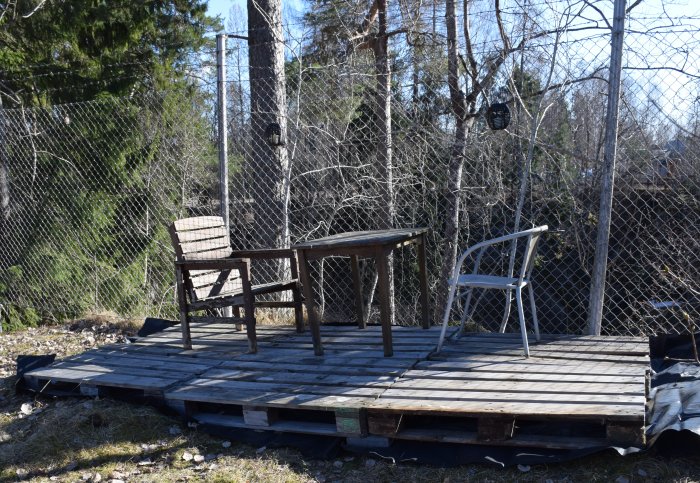 Nybyggd träbalkong med stolar och bord, säkert placerad innanför ett staket i trädgården.