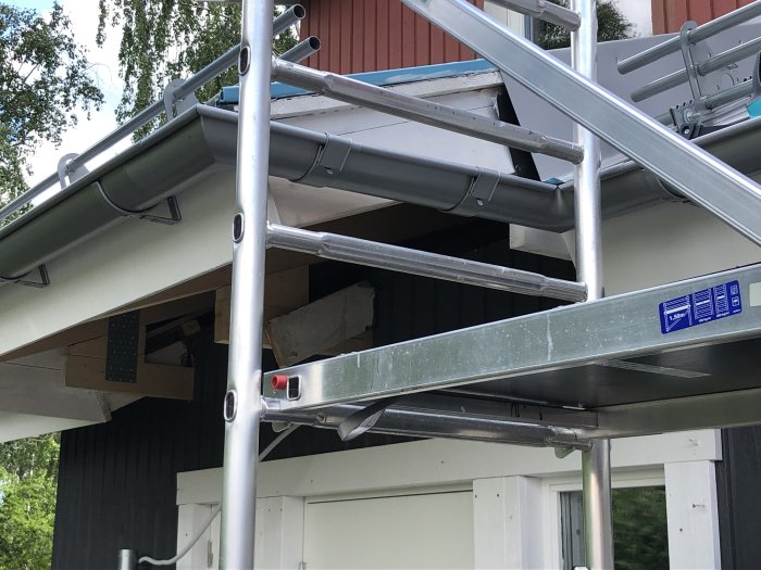 Sågade och målade brädor installerade bakom hängrännan på en husgavel, synliga från byggställning.