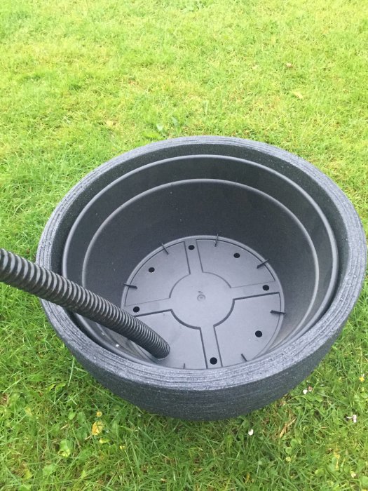 Självbevattnande kruksystem med plastkruka, odlingsfat och påfyllningsslang på grönt gräs.