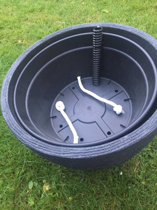 DIY självvattnande kruksystem med omvänd blomkruka, odlingsfat, slang och repstumpar för bevattning.