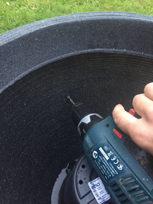 En hand håller en elektrisk borr för att borra ett hål i en självvattnande kruka för trädgårdsodling.