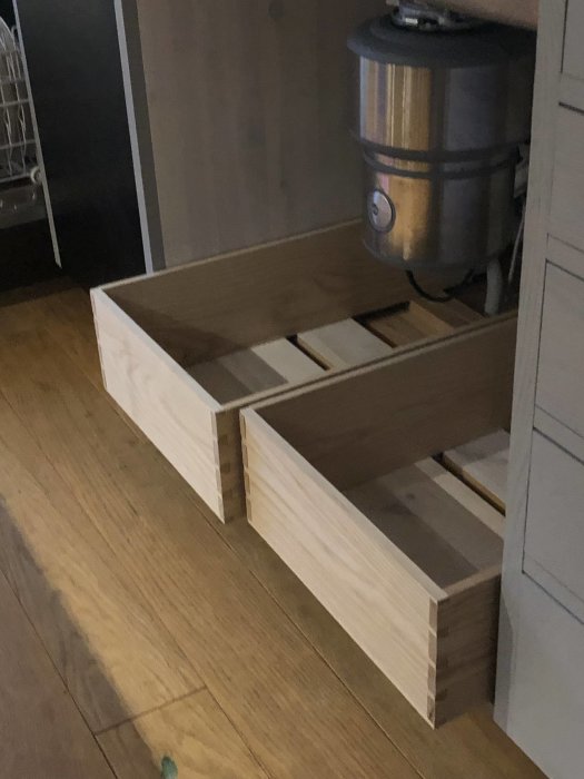 Trähörn av omonterad låda under konstruktion i ett kök, intill en diskmaskin.