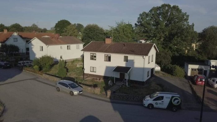 Aerial view of a residential area with a two-story house and vehicles parked along the street.