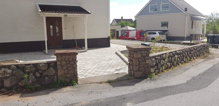 Renoverat hus med ny stenlagd uppfart och stensatt mur längs trottoarkanten.