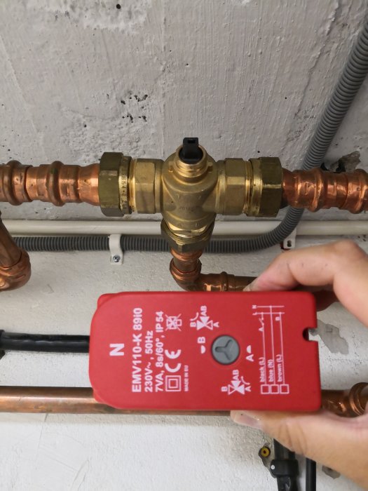 Hand håller en ventilmotor framför en växelventil i en installation för vattenvärmesystem.