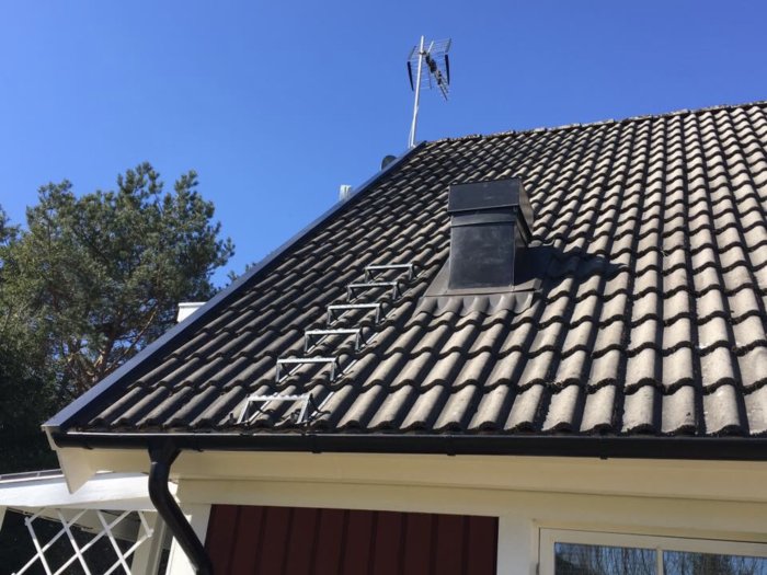 Skorsten med måttet 400x400 mm på ett svart tegeltak, under blå himmel, bredvid en TV-antenn.