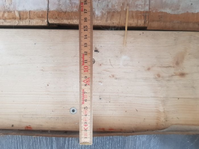 Breddmätning av ett trägolv med måttband som visar 155 mm, intill gammal väggkonstruktion.