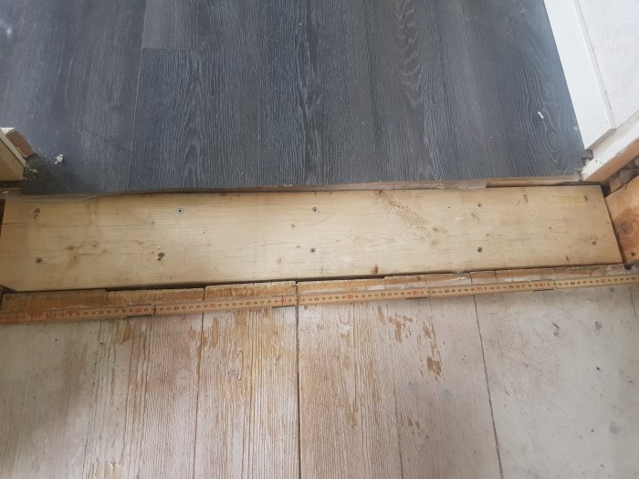 Breddmått av hålet mellan vardagsrum och köks golv med synlig tröskel och ojämnt golv.