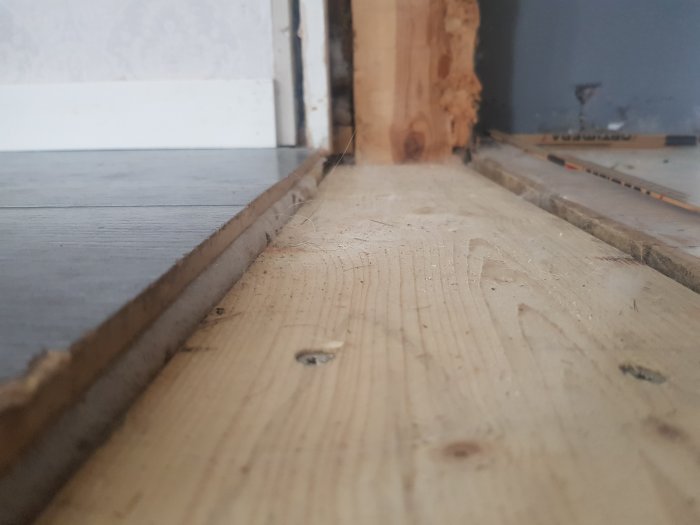 Golvvyn av ett bredt, ojämnt hål där en skjutdörr mellan vardagsrum och kök varit, med synliga ändar av trägolv och karm.