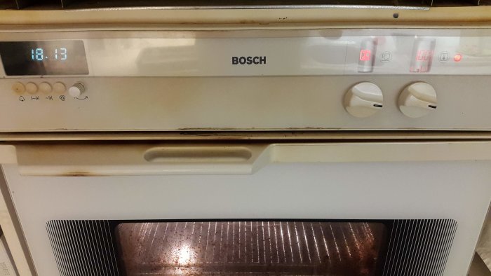En beige Bosch-ugn från 90-talet med digital klocka visande tiden 18:13 och röda indikatorlampor, termostatvred syns.
