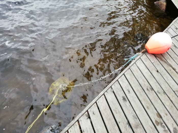 Nyinstallerad bojsten under vatten med kätting och flytande röd boj brevid träbrygga.