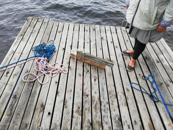 En person står på en träbrygga med rep och en sten med lyftögla och kätting.